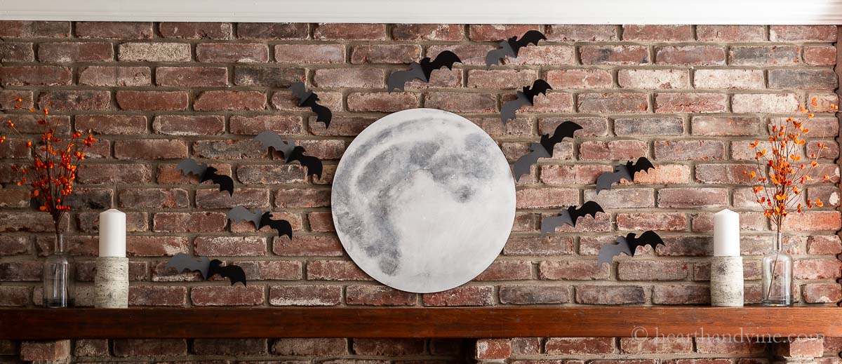 The finished Halloween decorated mantel with a large full moon and bats flying around.