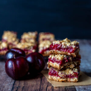 Stacked plum cobbler bars next to a few fresh plums.