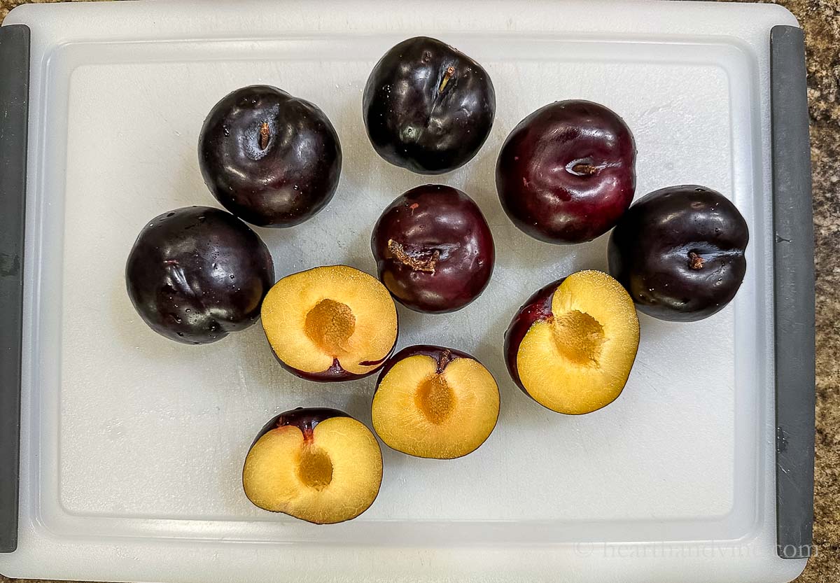 Small plums whole and sliced in half on a cutting board.