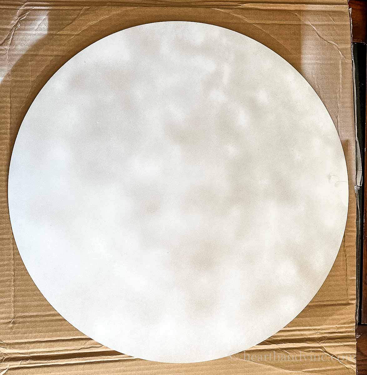 Large wooden round sprayed lightly with white spray paint.