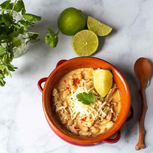 Bowl of creamy slow cooker white chicken chili with fresh limes and cilantro on the side.