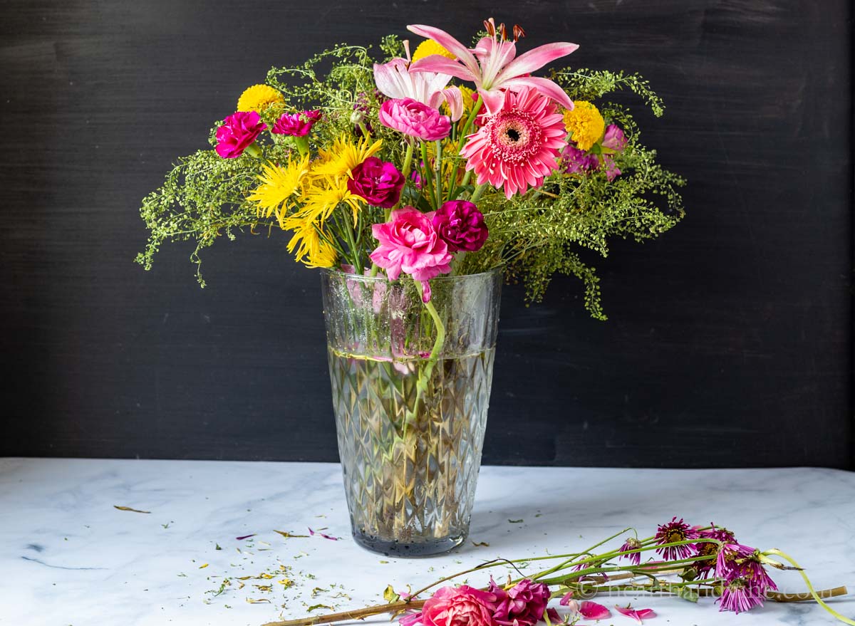 A more sparse looking flower arrangement with wilted flower and spent flowers on the table in front.