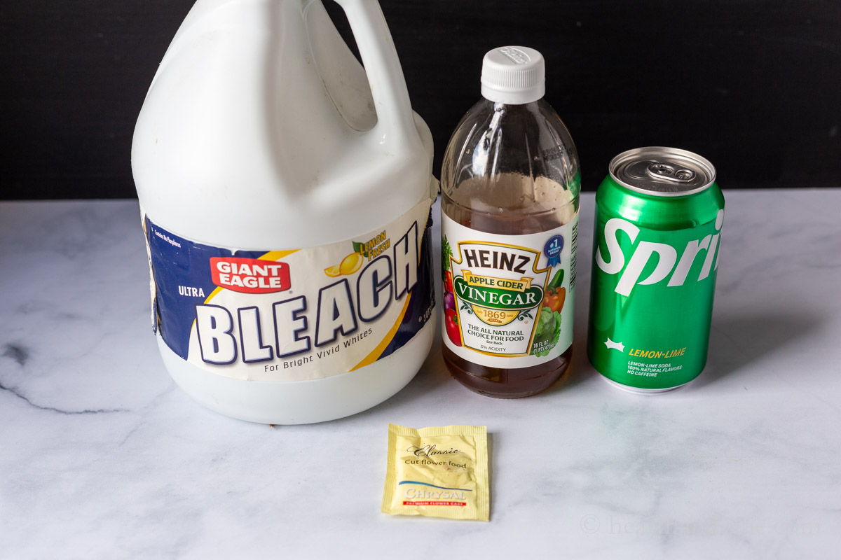 Bleach, cider vinegar, can of sprite and a flower food packet on a table.