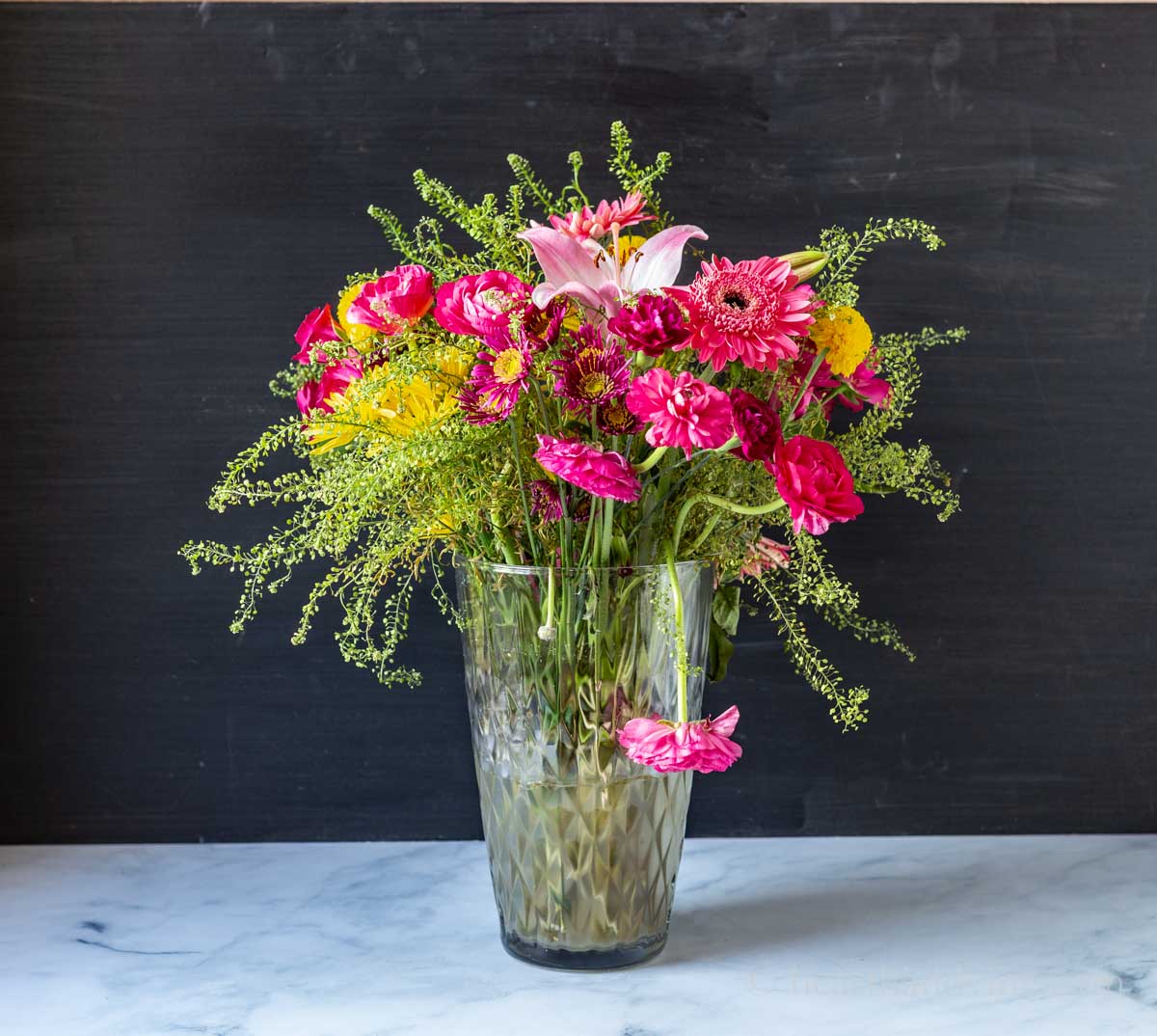 A flower arrangement in a large vase after seven days with a wilted ranunculus in front.