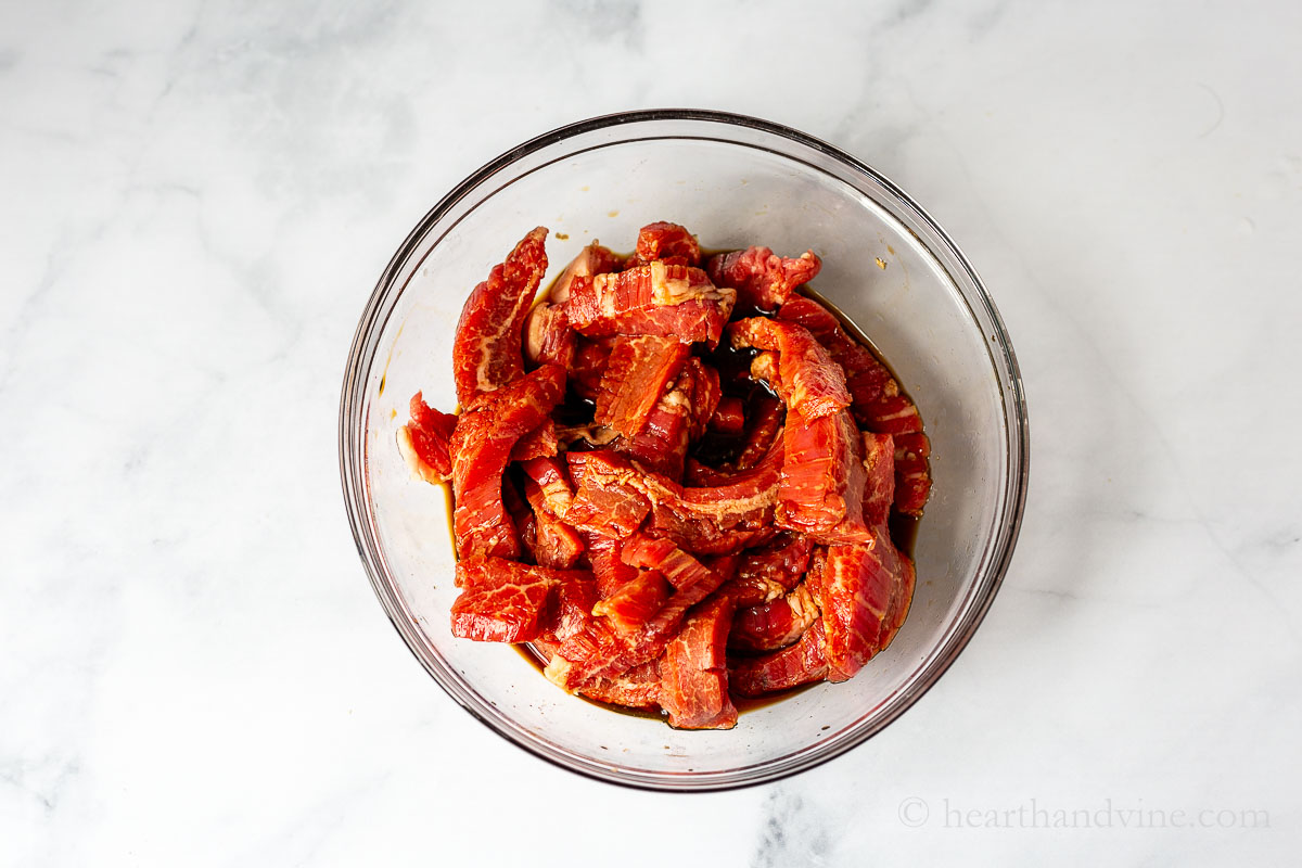 Strips of flank steak in a bowl with marinade.
