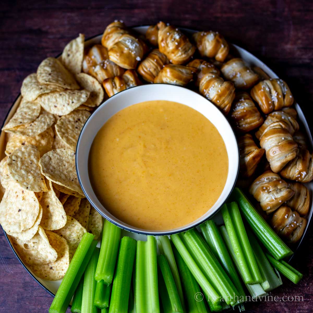 Bowl of beer cheese dip surrounded by pretzel bites, tortilla chips and celery sticks.