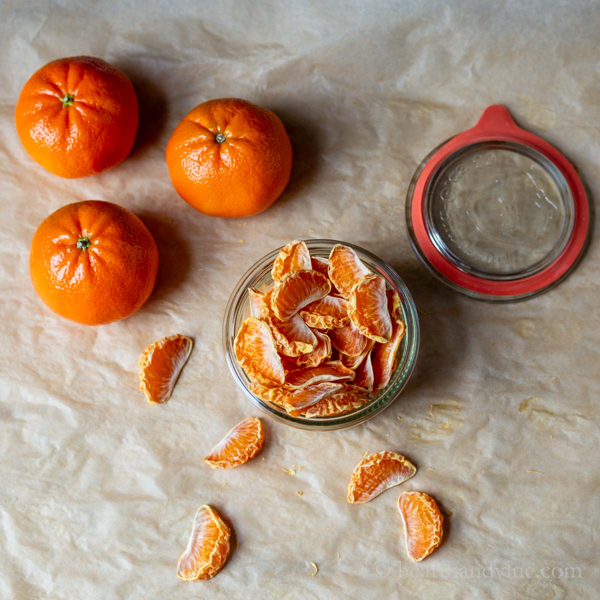 Jar of dried mandarin oranges with a few fresh unpeeled mandarins on the side.