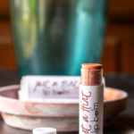 Tube of lip balm standing up with cap off in a red shade with Just a Hint label.