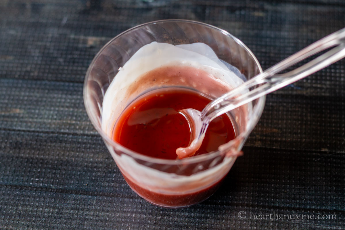 DIY tinted lip balm ingredients melted together in a plastic cup with a plastic spoon.