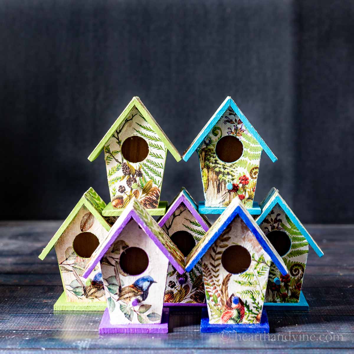 Seven decoupaged bird houses in different colors.