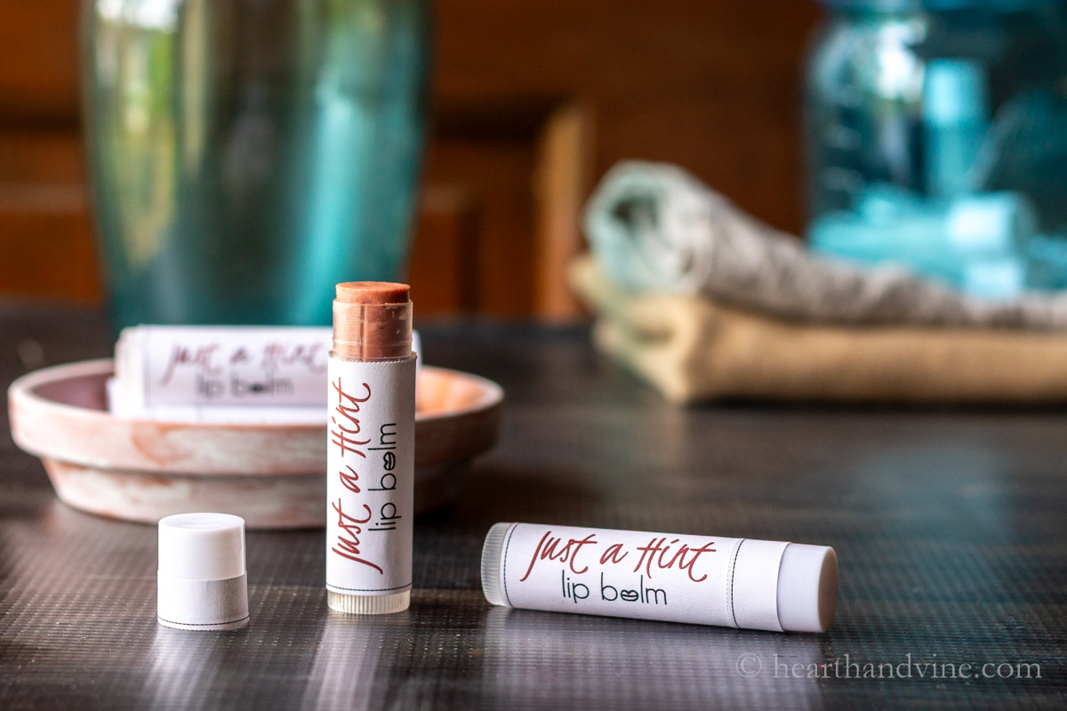 A tube of tinted lip balm with the cap off next to another tube with the cap on laying on its side.