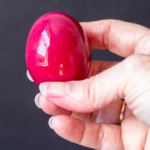 A hand holding up a dark pink red beet picked egg.