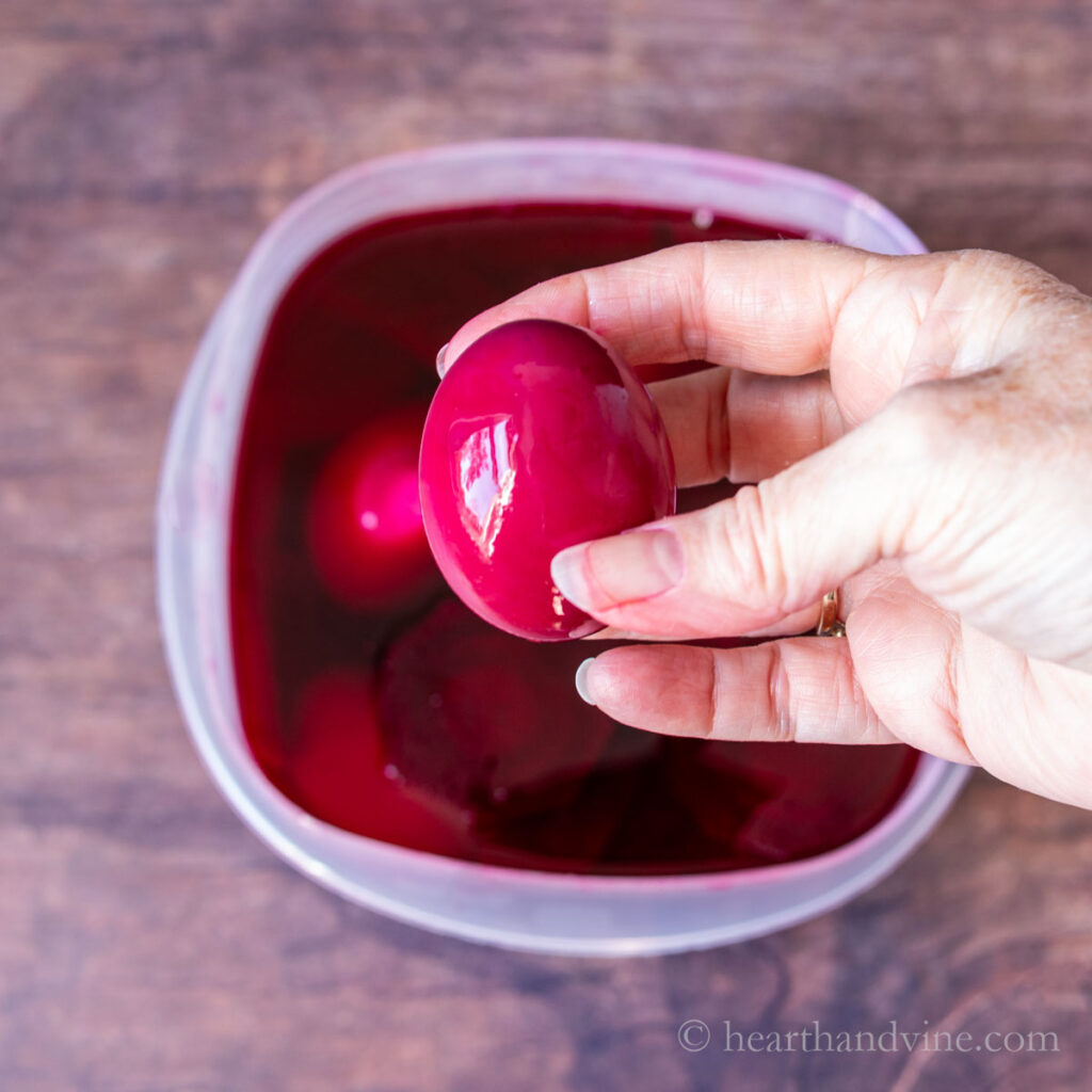 A hand holding a red beet pickled egg.
