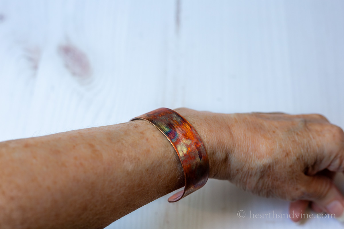 A flame painted copper cuff bracelet on a wrist.