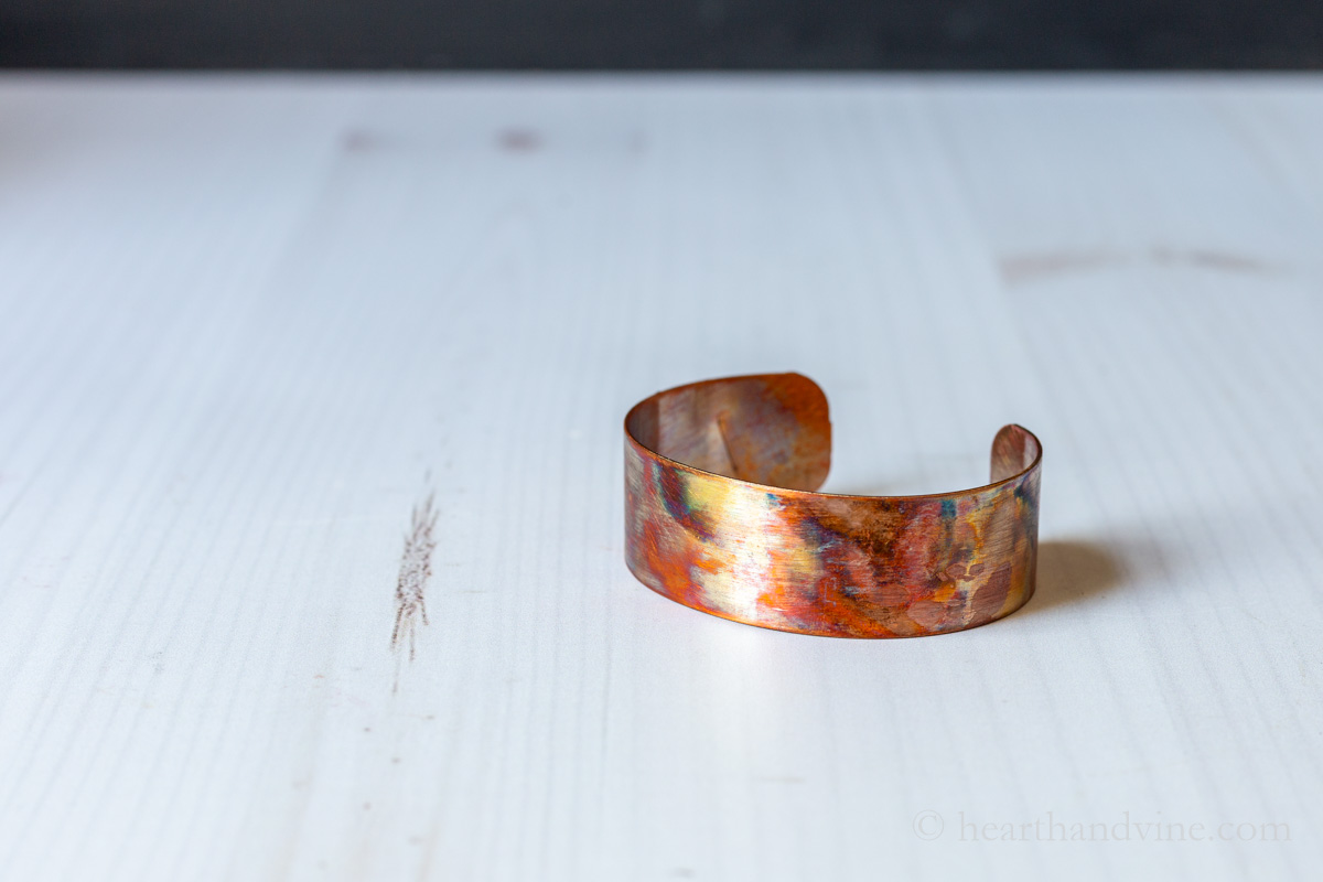 The flame painted copper cuff on a table.