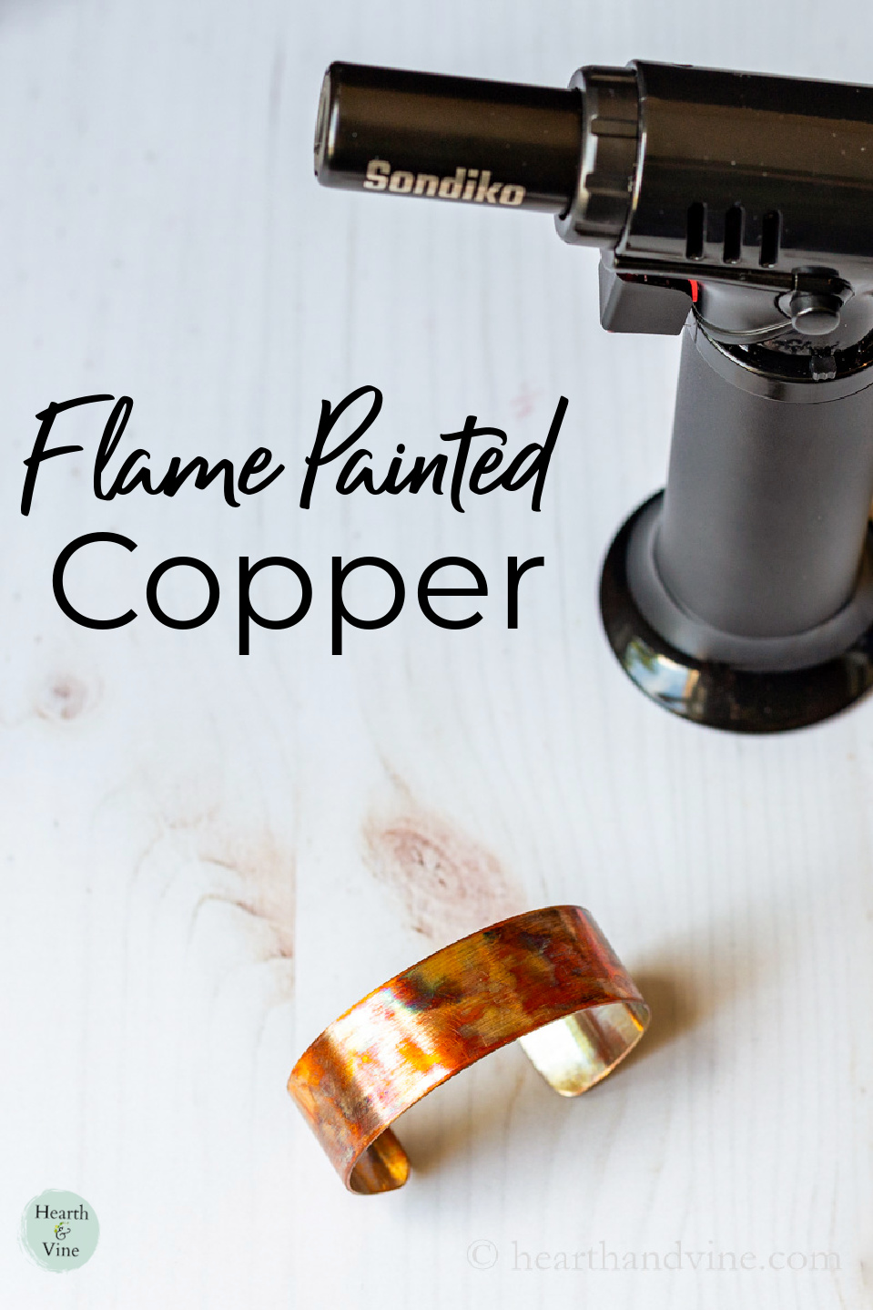 A flame painted copper cuff bracelet next to a kitchen torch.