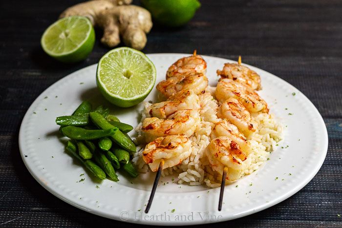 Grilled shrimp on wooden skewers over rice with snap peas and a half lime on the side.