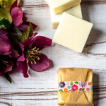 A few square lotion bars next to one that is wrapped in brown paper with floral washi tape.