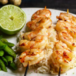 Close view of grilled lime shrimp skewers on a bed of rice with a half lime and snap peas.