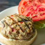 Close up of a southwest turkey burger with the top bun on the side and a slice of tomato.
