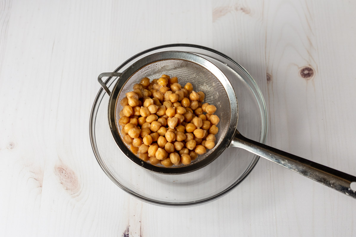 Chickpeas in a mesh strainer over a clear bowl.