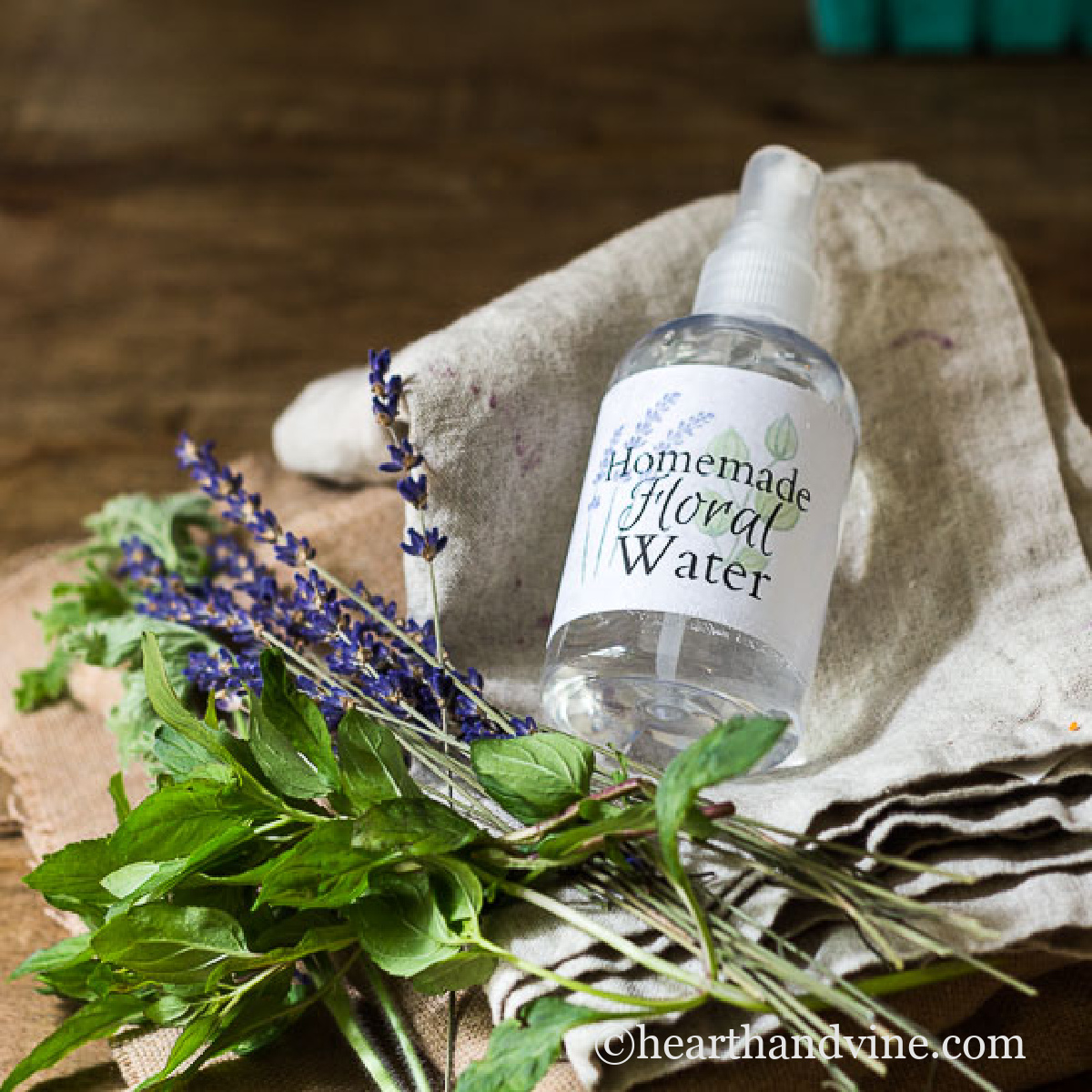 Spray bottle of an herbal infusion or floral water lying on a linen napkin next to some mint and lavender.