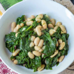 A serving bowl of beans and greens with Swiss Chard on a colorful napkin.