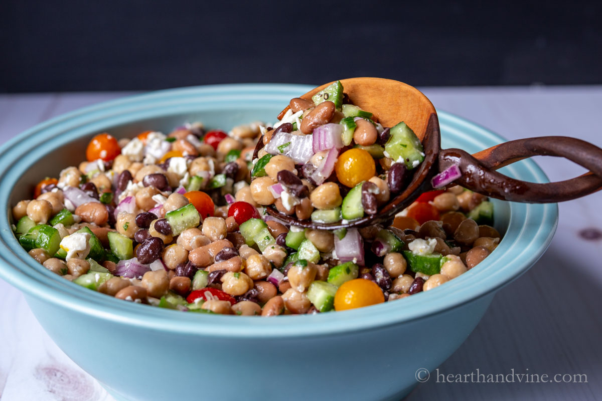 A large wooden serving spoon lifting out a serving of a dense bean salad.