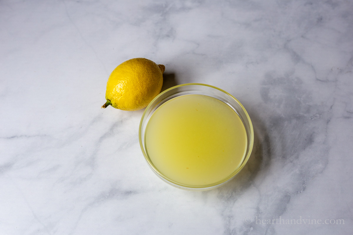 Bowl of lemon juice and a whole lemon on the side.