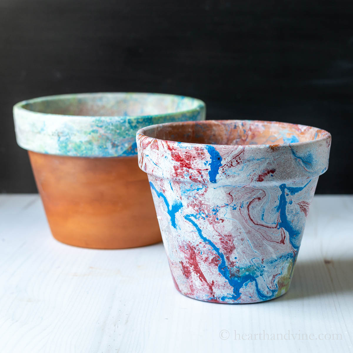 Two marbled terracotta pots. One with a blue and green painted rim and the other fully painted with red, white and blue paint.