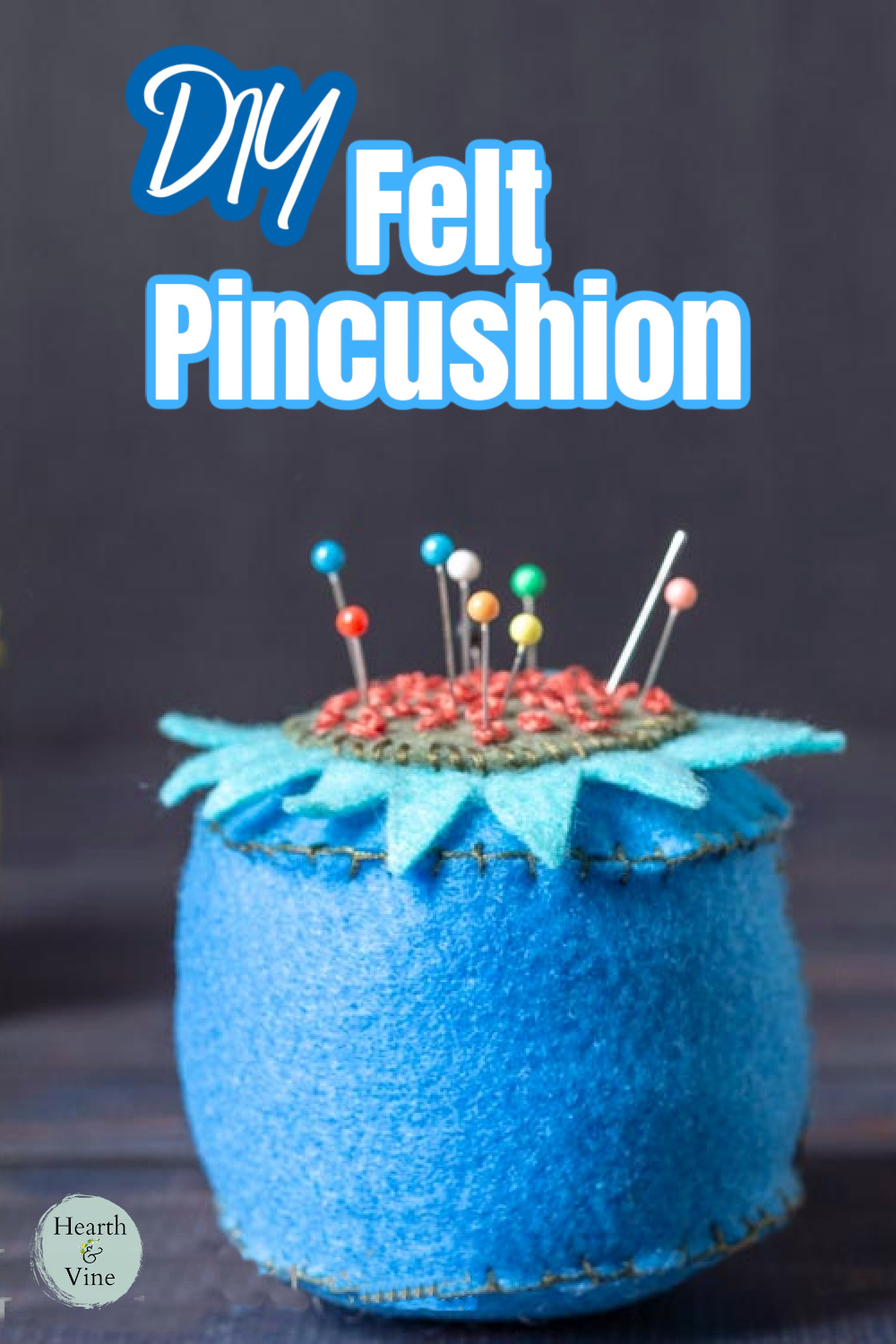 Blue felt pin cushion with a flower top and embroidery accent. Colorful pins in the top.