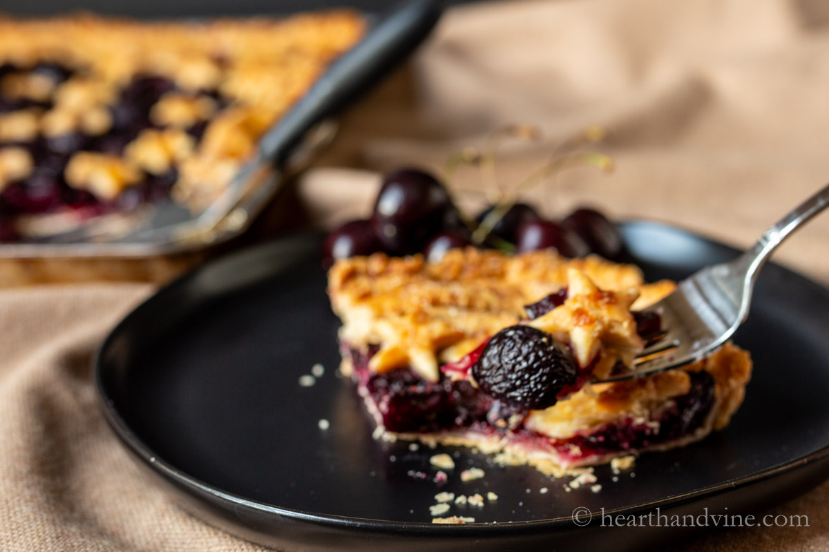 Serving of cherry slab pie with a fork lifting a bite.