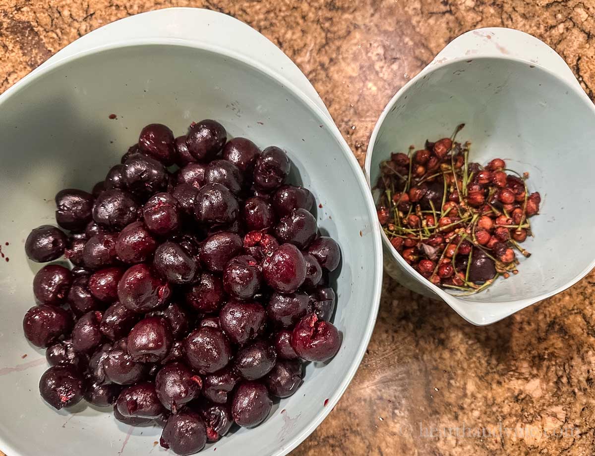 Two bowls. One with pitted cherries and one with the stems and pits.
