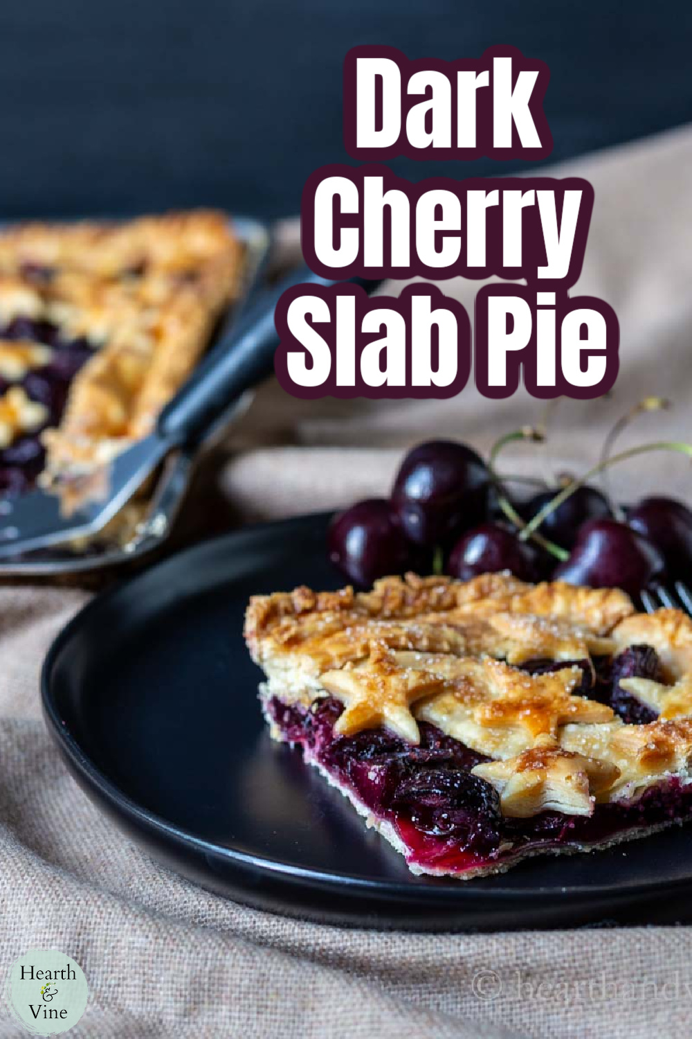 Corner serving of a cherry slab pie on a black plate with a few fresh cherries.