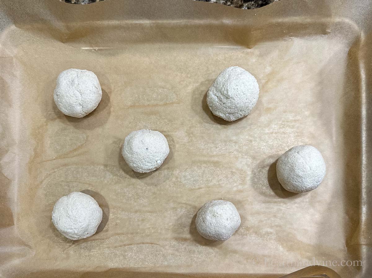 Balls of bagel dough on a parchment lined baking sheet.