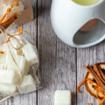 Aerial view of a wax burner, a couple of wax cubes, a bag of the wax melts and thin orange rind peels.