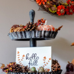 Thrift store handmade tiered tray decorated for fall with pine cones a "hello fall" sign and pumpkins.