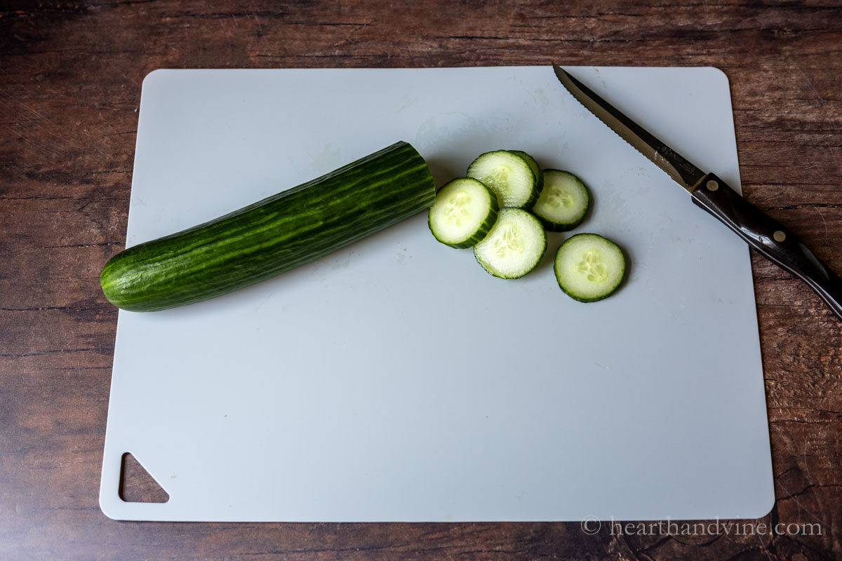 A English cucumber sliced on a cutting board with a serrated knife.