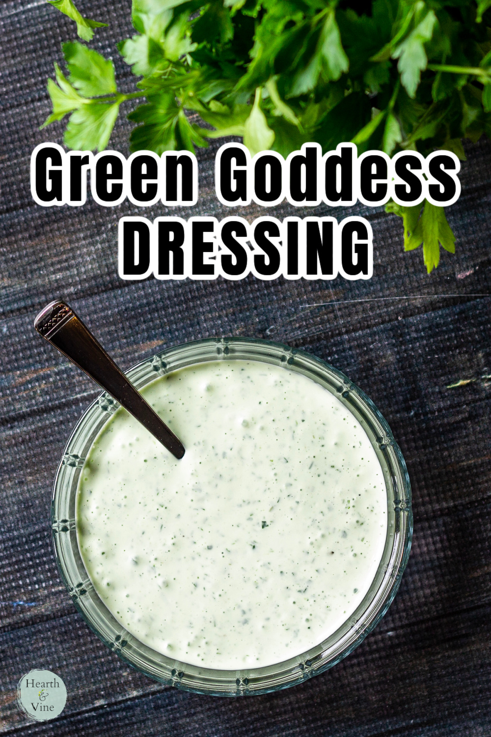 A bowl of green goddess dressing with a spoon and fresh parsley in the background.