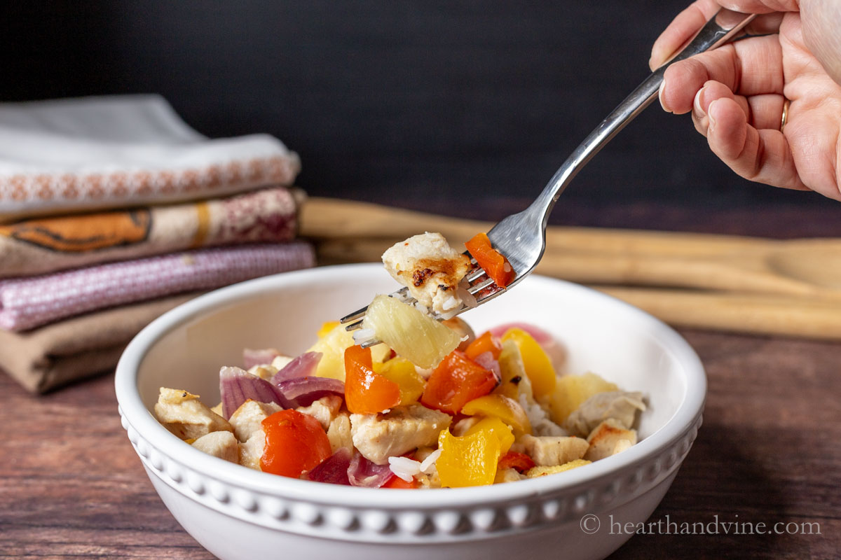 A fork lifting a bite of Hawaiian chicken dinner from a bowl.