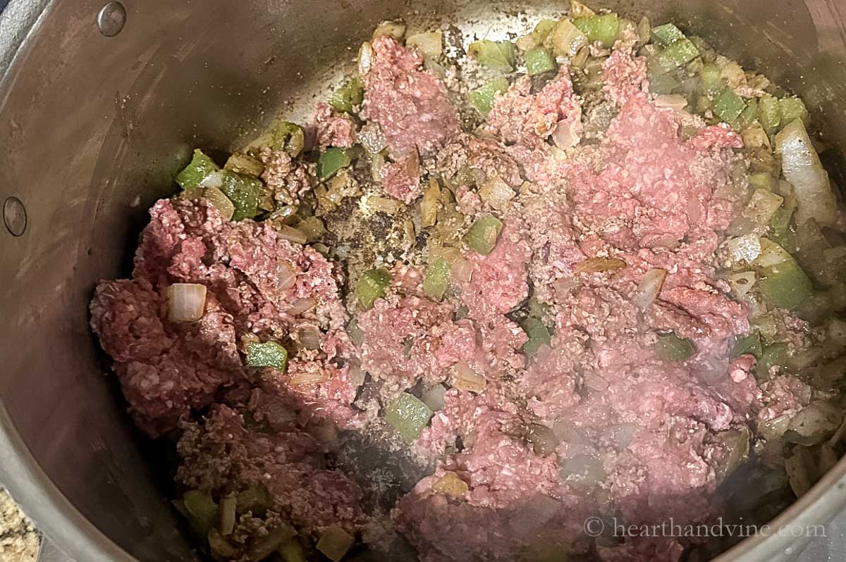 Ground beef added to vegetables and spices in a large pot.