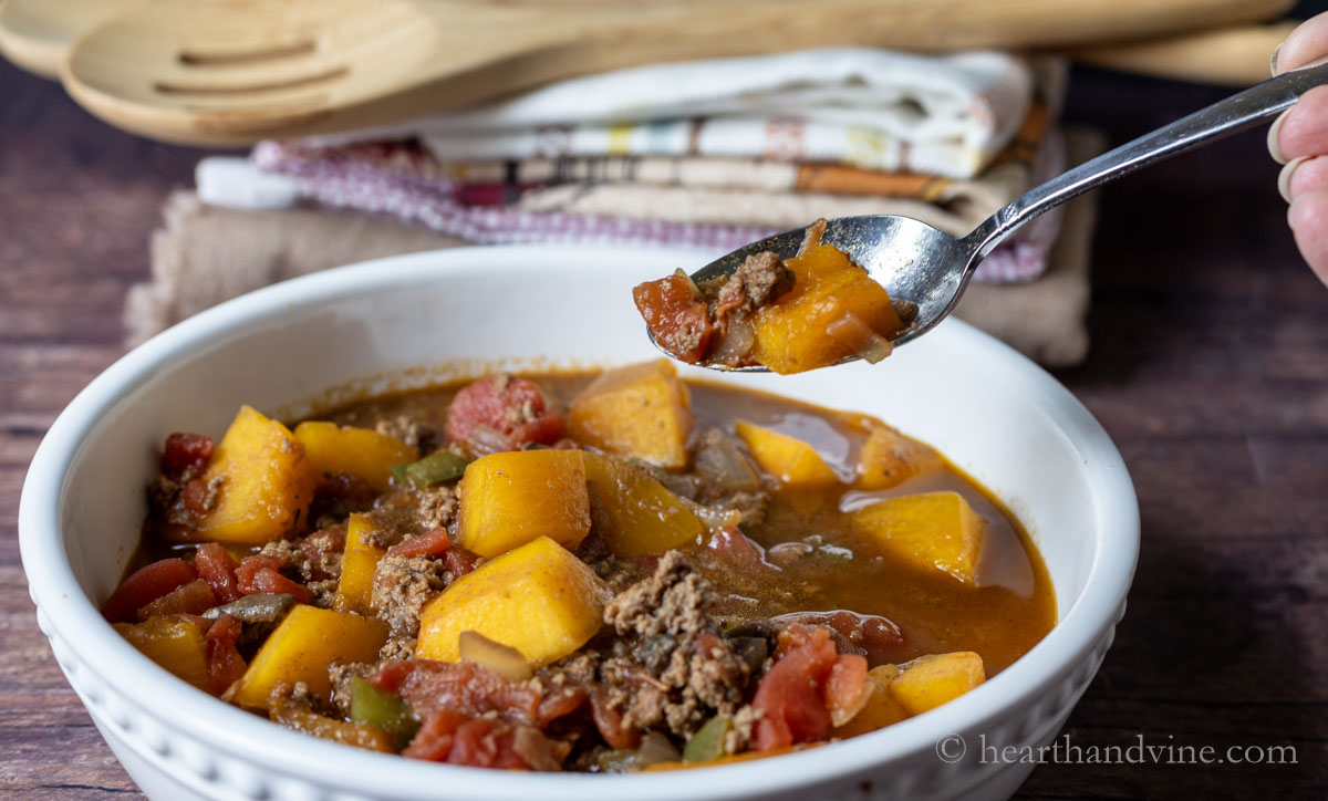 A spoon lifting a bit of the pumpkin chili from a serving bowl.