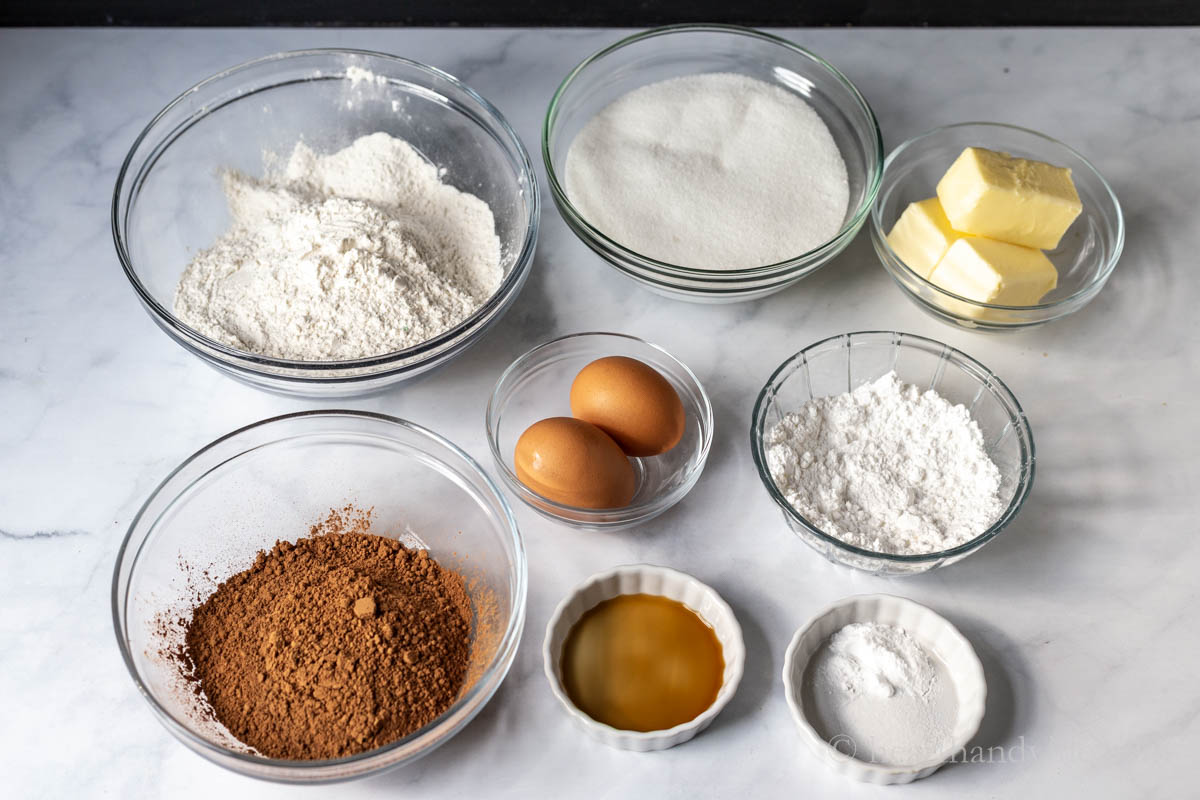 Ingredients for the chocolate crinkle cookies including, flour, sugar, cocoa, butter, eggs, vanilla, baking soda, and powdered sugar.