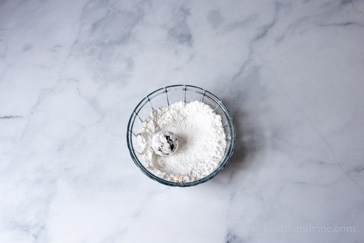 A small bowl of powdered sugar with a ball of cookie dough.