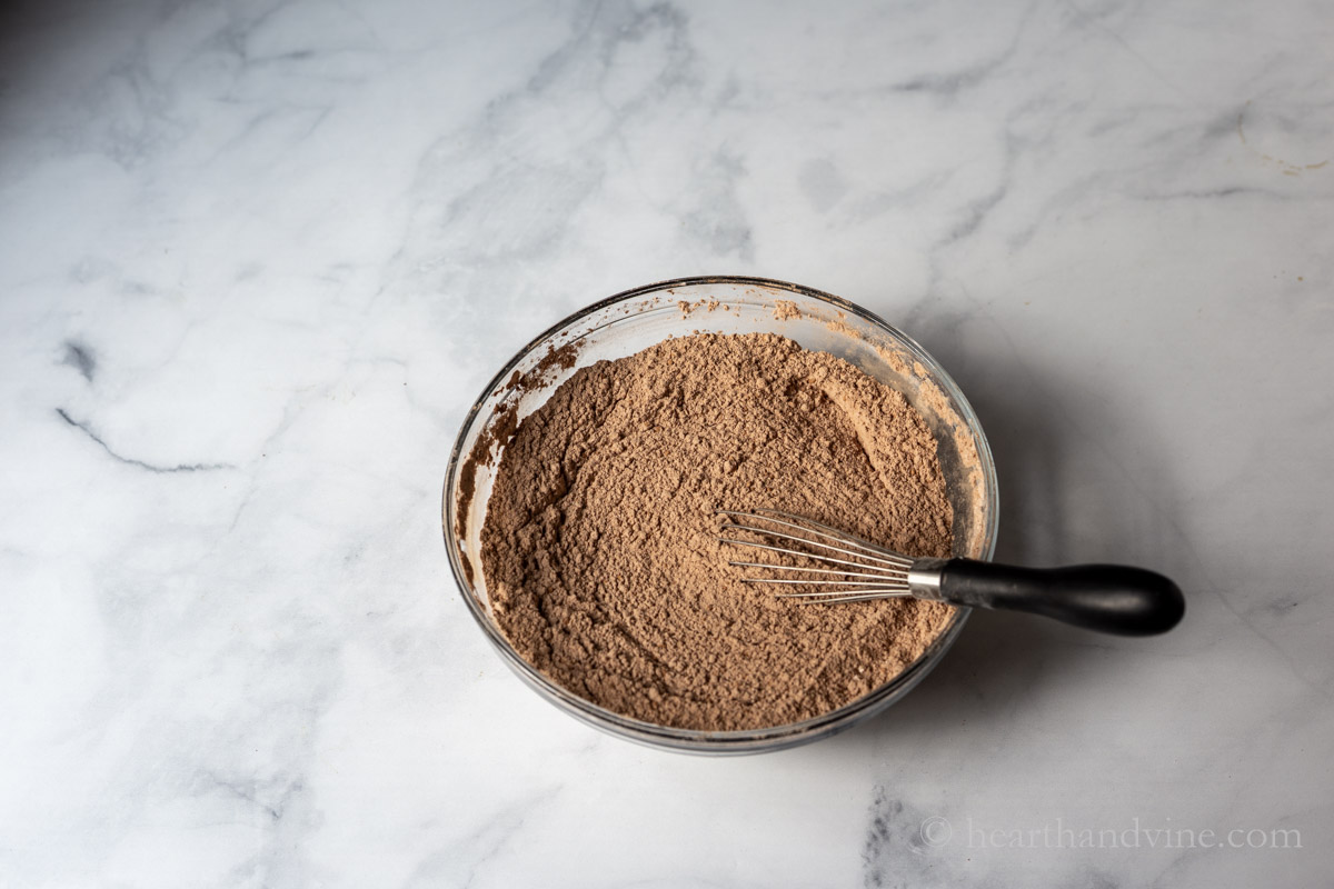 Dry ingredients in a bowl with a whisk including flour, cocoa, baking soda and salt.