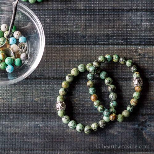 two healing stone bracelets in green shade next to a bowl of beads.