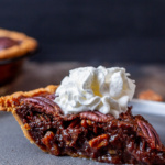 Slice of chocolate pecan pie with whipped cream on top.