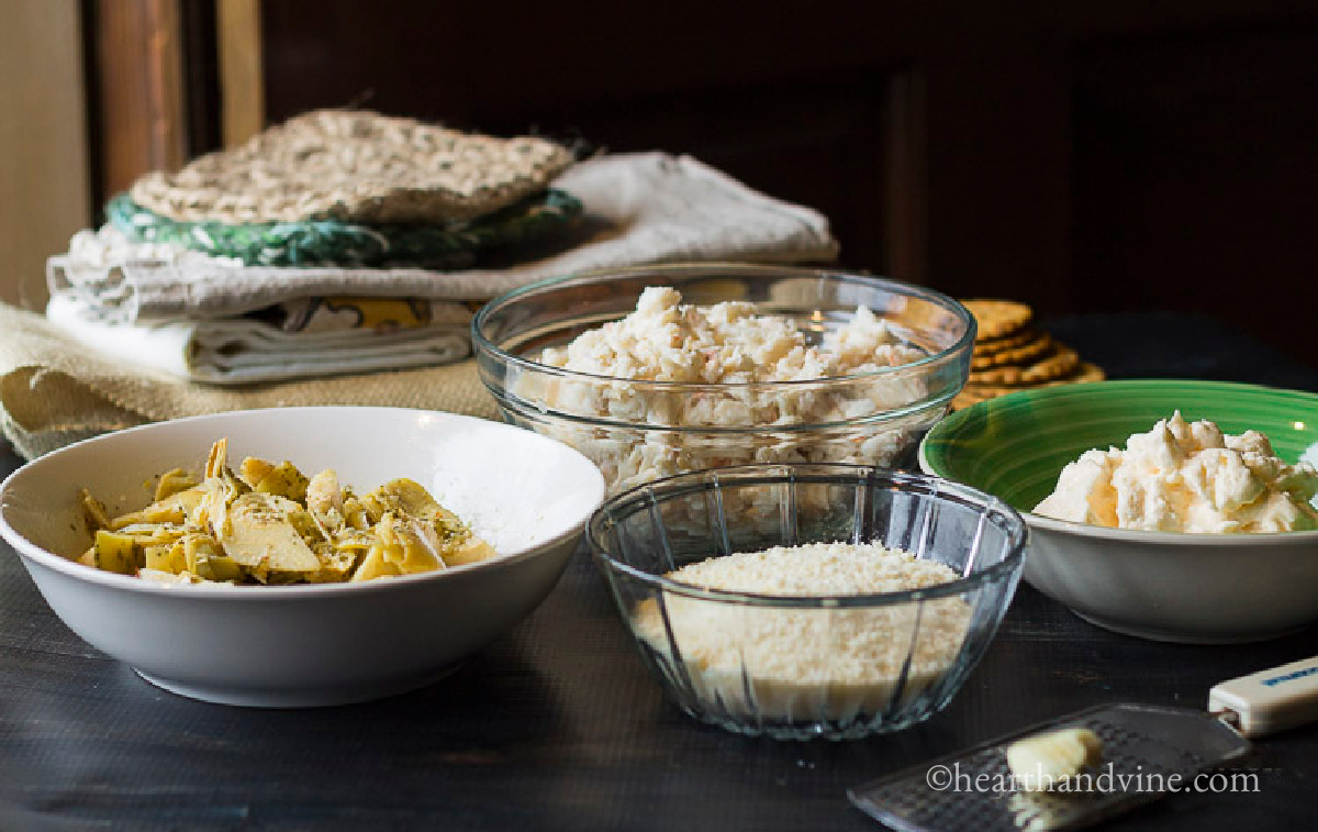 Ingredients for a hot cheesy crab and artichoke dip including, mayo, parmesan cheese, canned artichoke hearts, crabmeat and garlic.