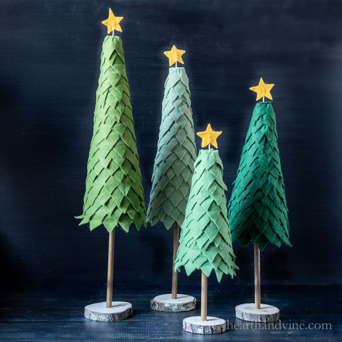 Four felt Christmas trees on a table.