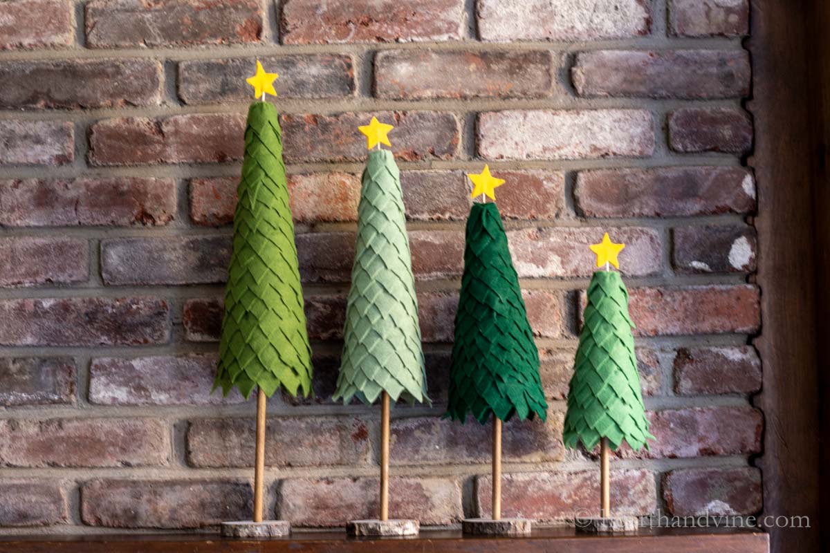 Four different shades of green felted trees with yellow stars on top on a mantel.